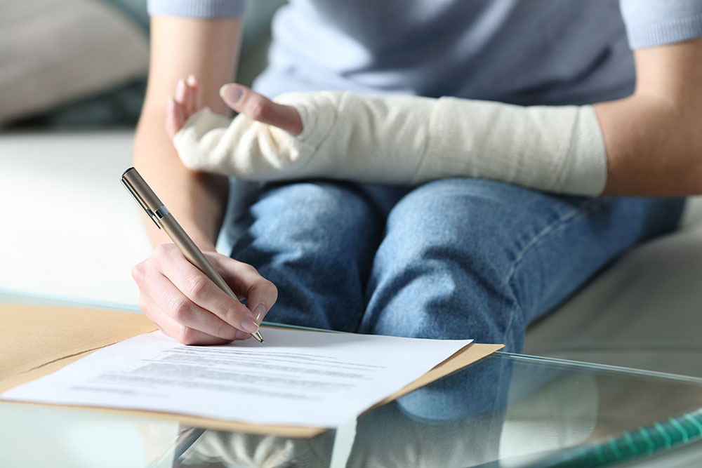 A woman with a bandaged arm signs legal paperwork.